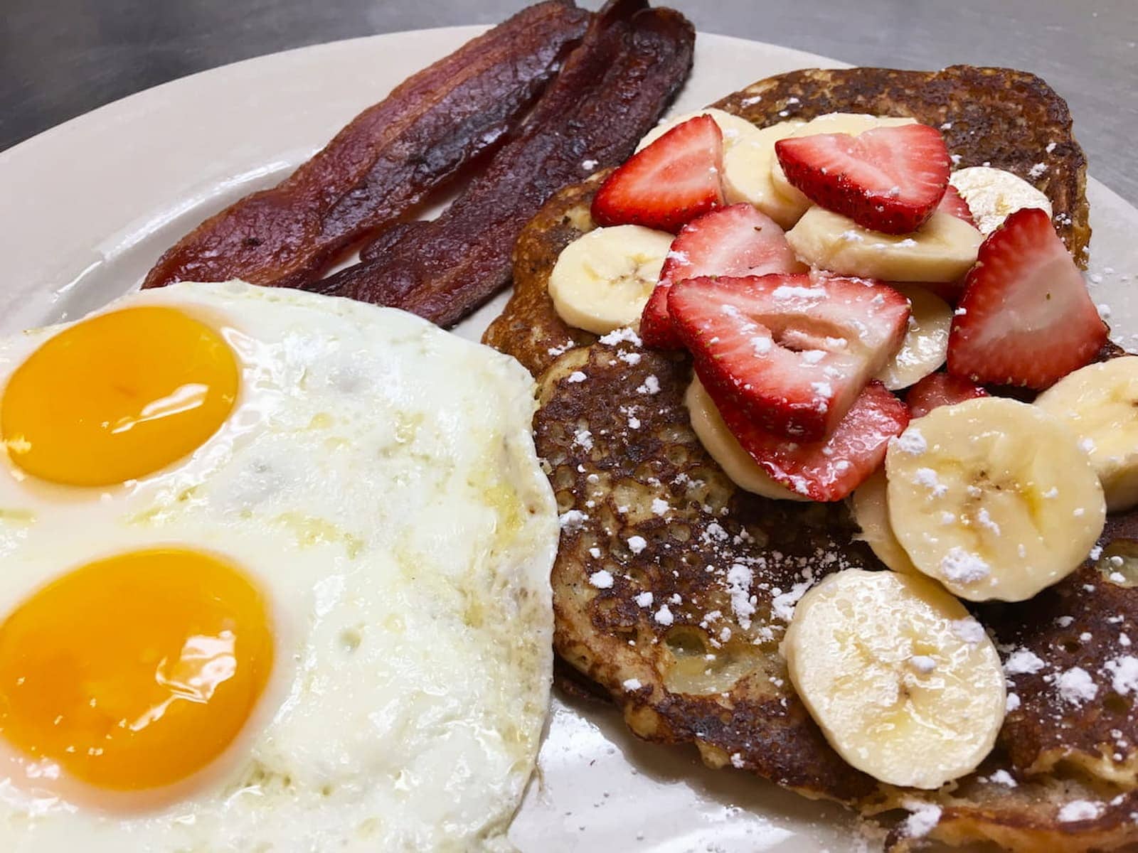 French toast croissant topped with strawberries and bananas, served with bacon and sunny-side-up eggs at Bailey's Breakfast & Lunch in Omaha